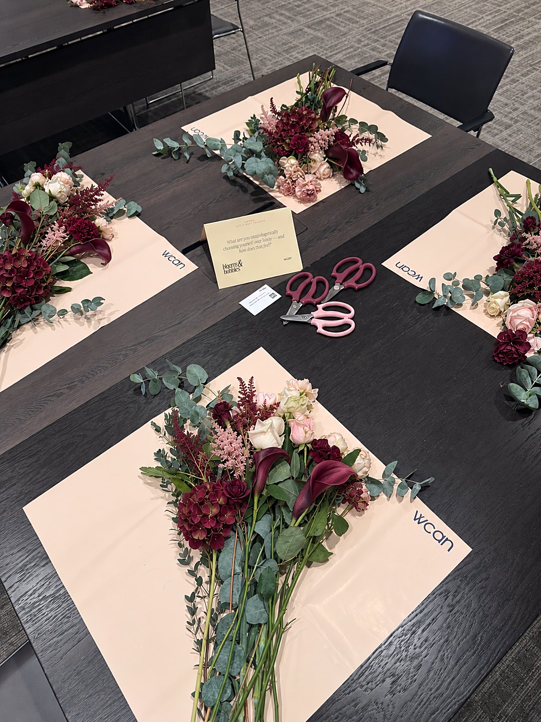 Place settings for Bloom & Bubbles: WCAN mats with burgundy calla lilies, hydrangea, roses, astilbe and eucalyptus on a dark table
