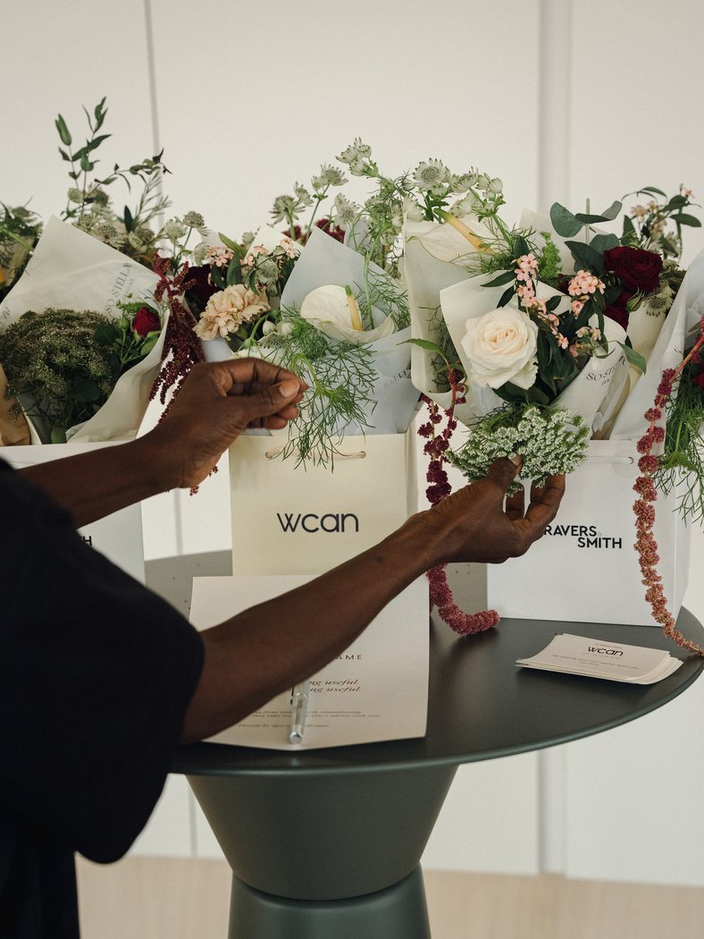 Hands arranging a bouquet over a WCAN and Travers Smith gift bag