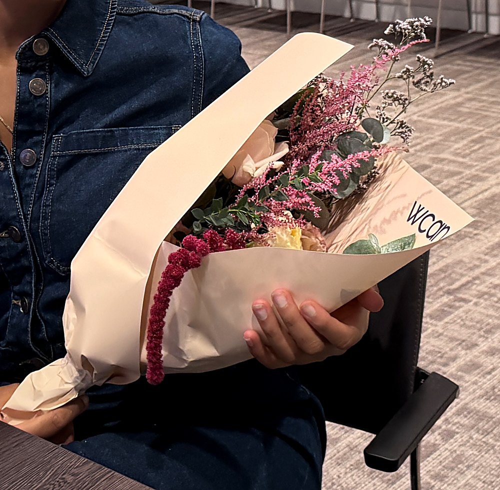 A guest holding her finished hand-tied bouquet, wrapped in WCAN paper