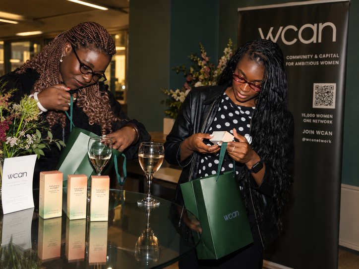 Two women opening green WCAN gift bags, glasses of wine on the table